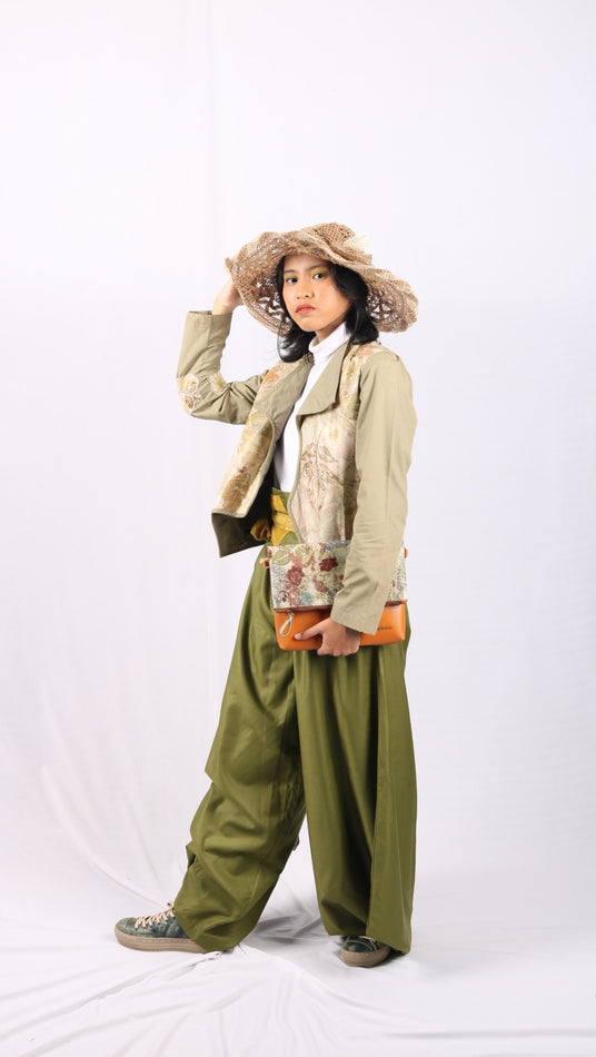 Person wearing a beige coat, green pants, and a patterned hat on a white background
