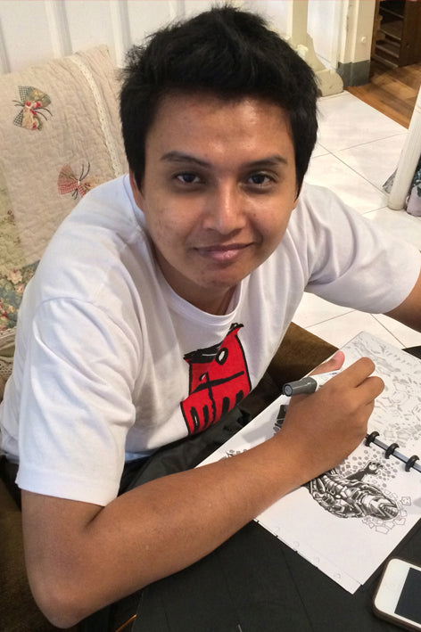 Person sitting at a table with a tattoo design and phone, wearing a white t-shirt with a red graphic.